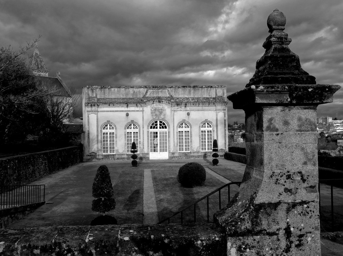 Un pavillon éclairé par le soleil couchant sur fond d'orage menaçant. Un jardin à la française, bien ordonné. Au premier plan, sombre, le mur d'enceinte et un pilier. Au fond, à droite, Limoges moderne.